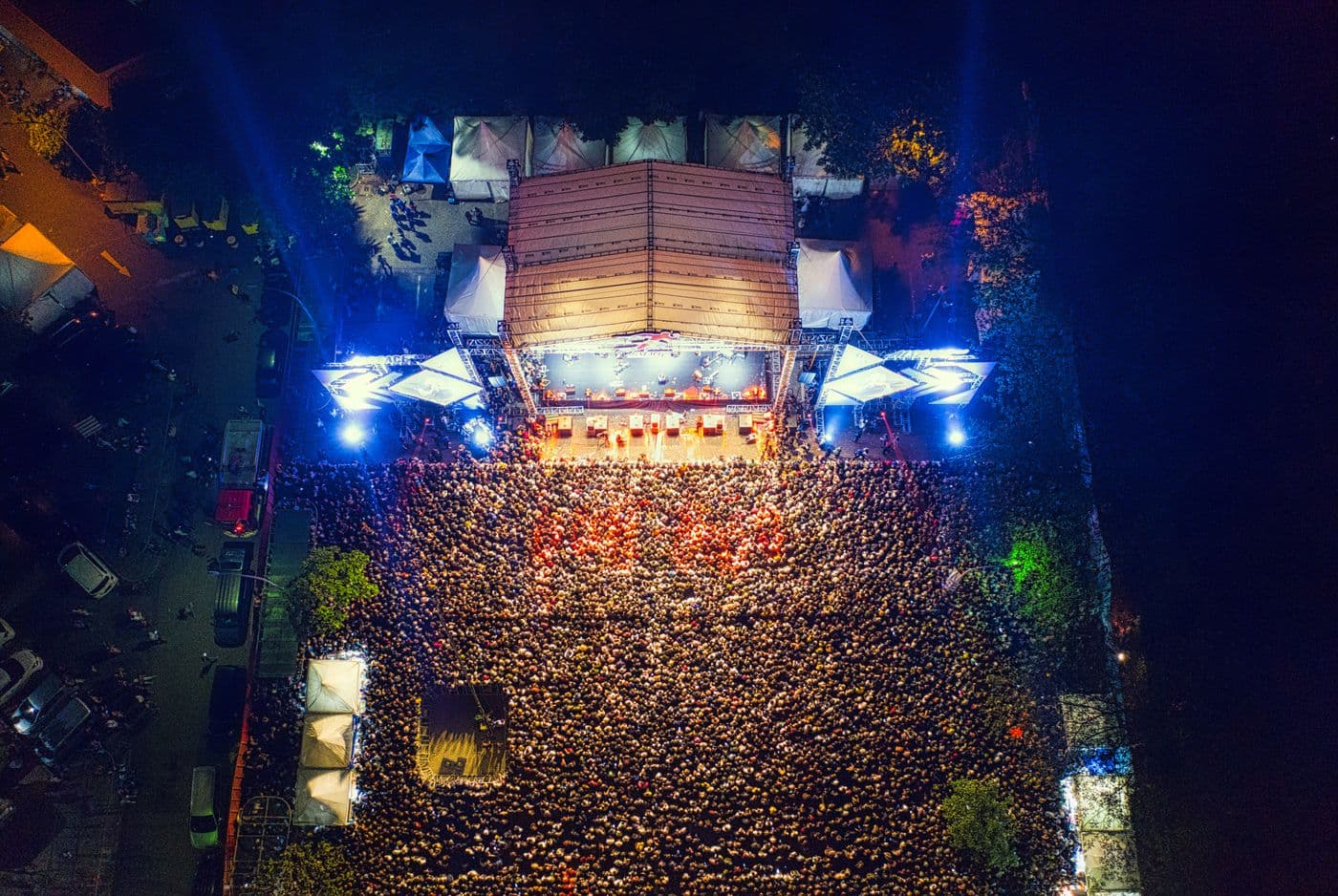 Vue aérienne d'un concert en plein air : une scène éclairée et une foule dense devant elle, de nuit